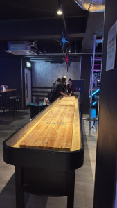 boom-battle-bar-cambridge-msrc-winter-party-2025-11-20-14.11.03-169x300 这个游戏也有意思，就是两个团队（粉色/蓝色）分别 从一头扔一个很滑的圆饼，掉下去0分，停下越远得分越高，可以把对手的圆饼打下去。 