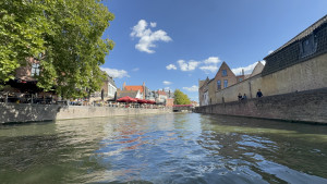 belgium-bruges-canal-cruising-2025-08-24-15.42.55-300x169 阳光下的布鲁日运河，两岸的露天餐厅、老城建筑与蓝天倒映在水面上。 